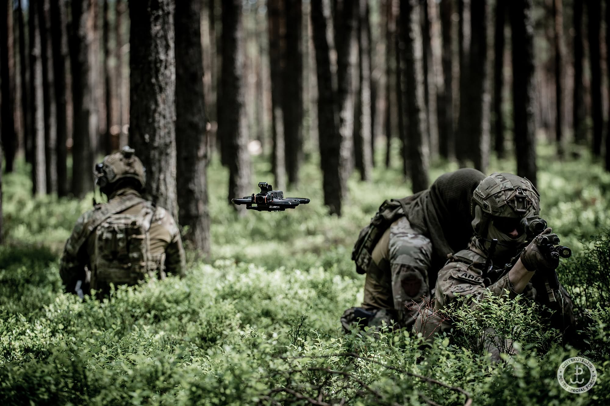Dwaj operatorzy JWK w lesie, dron FPV zawisa między nimi podczas rozpoznania