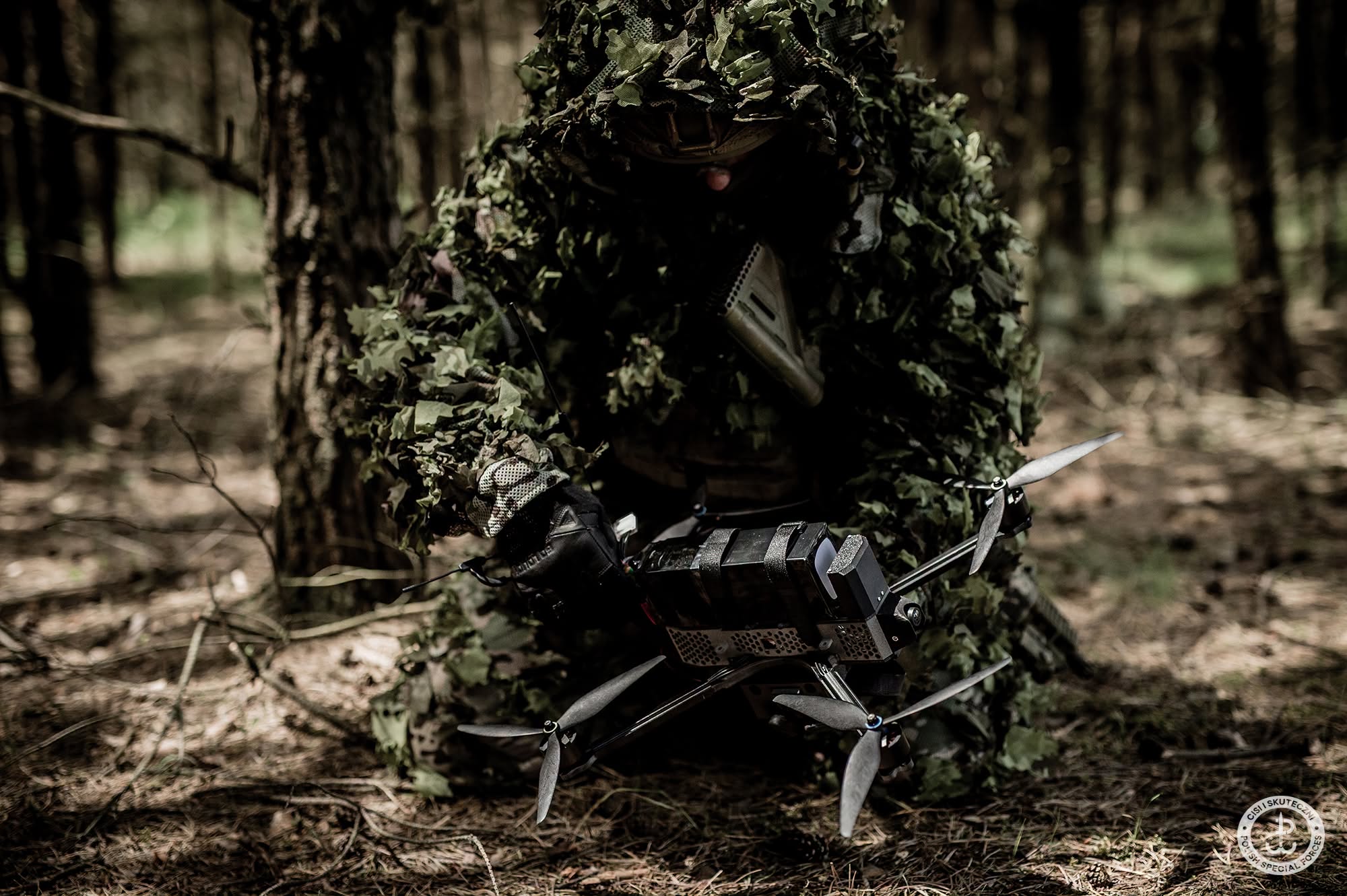 Operator JWK w maskowaniu ghillie przy dronie FPV ustawionym na plecaku