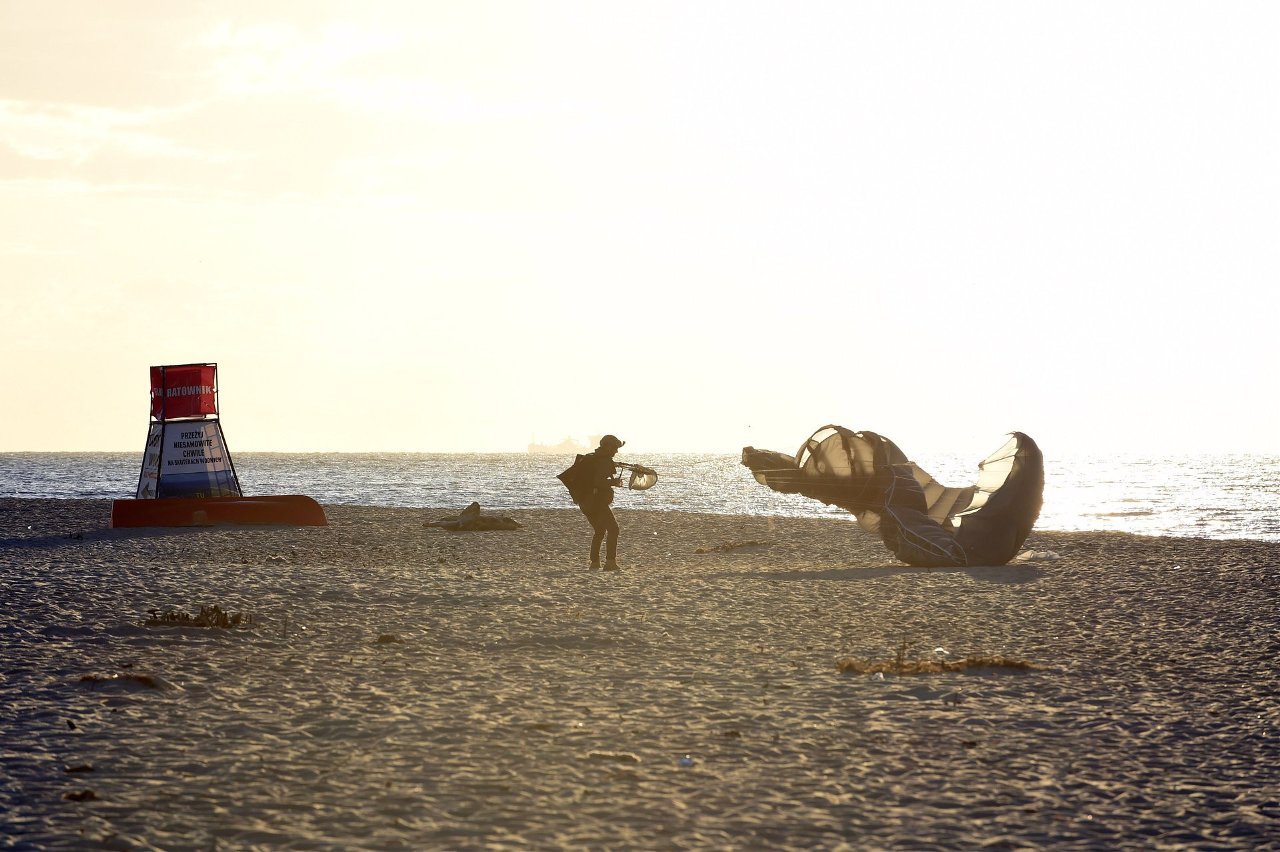 Żołnierz zwija czaszę spadochronu na pustej plaży pod słońce, obok wieża ratownika