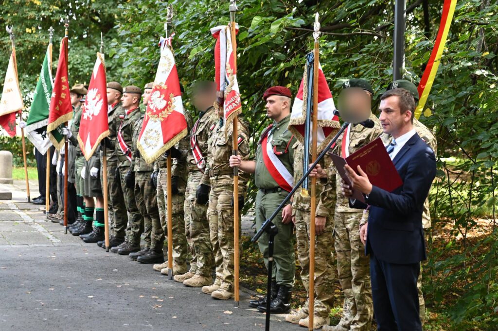 Szereg pocztów sztandarowych — wojskowych i harcerskich — ustawionych wzdłuż parkowej alei