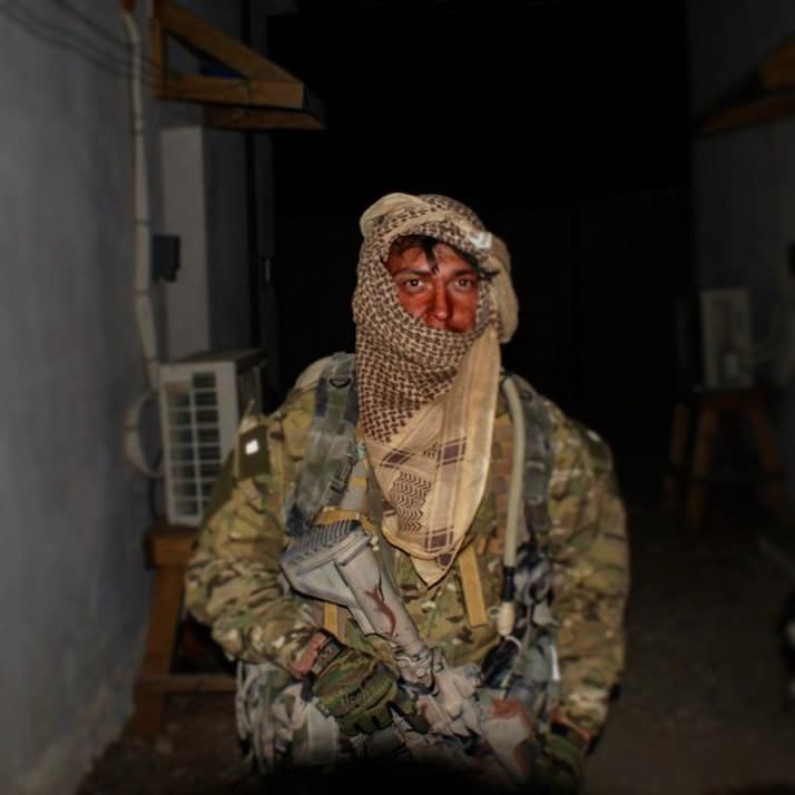 Żołnierz w mundurze multicam z szemagiem owiniętym wokół głowy, nocą we wnętrzu budynku