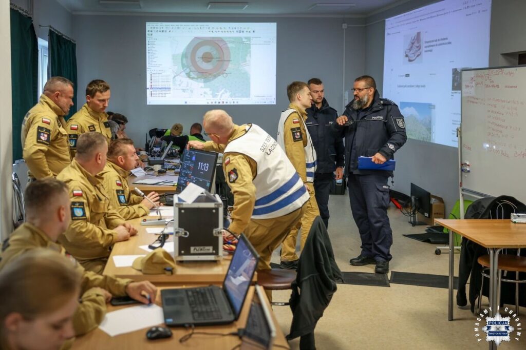 Sztab ćwiczeń: strażacy i policjanci przy stanowiskach z laptopami, na ekranie plan sytuacyjny