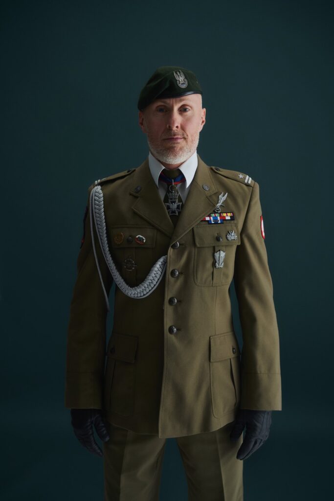 Mjr rez. Damian Matkowski w mundurze wyjściowym, sylwetka na ciemnym tle