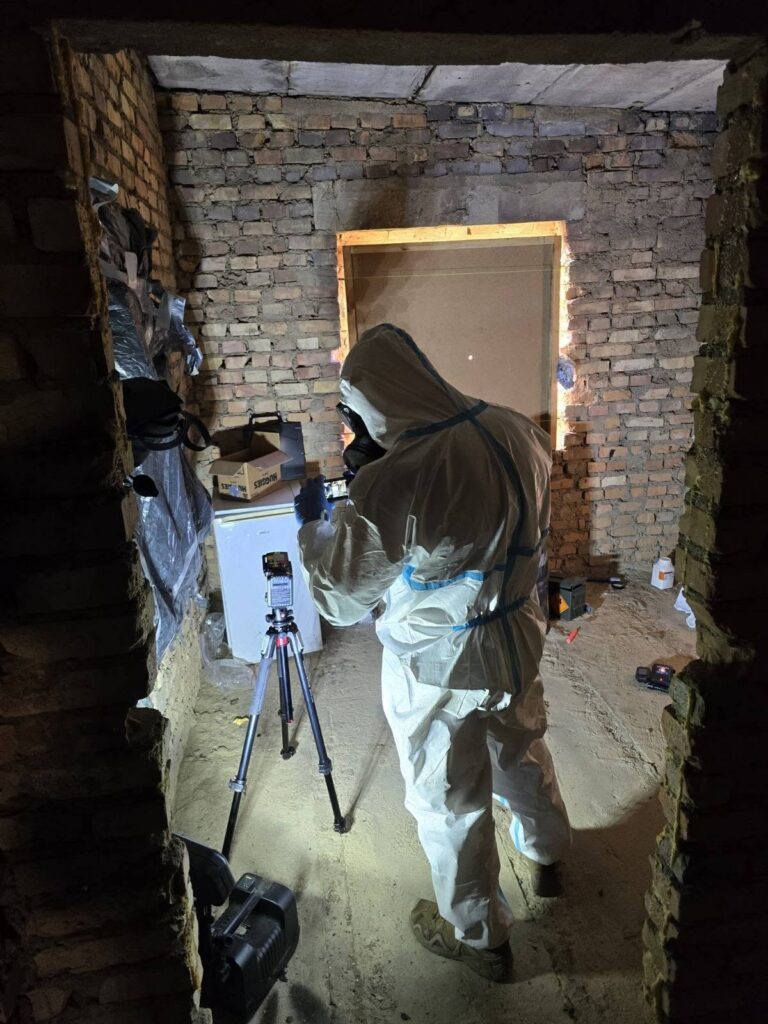 Uczestnik w kombinezonie ochronnym dokumentuje pomieszczenie z pozorowanym laboratorium materiałów wybuchowych