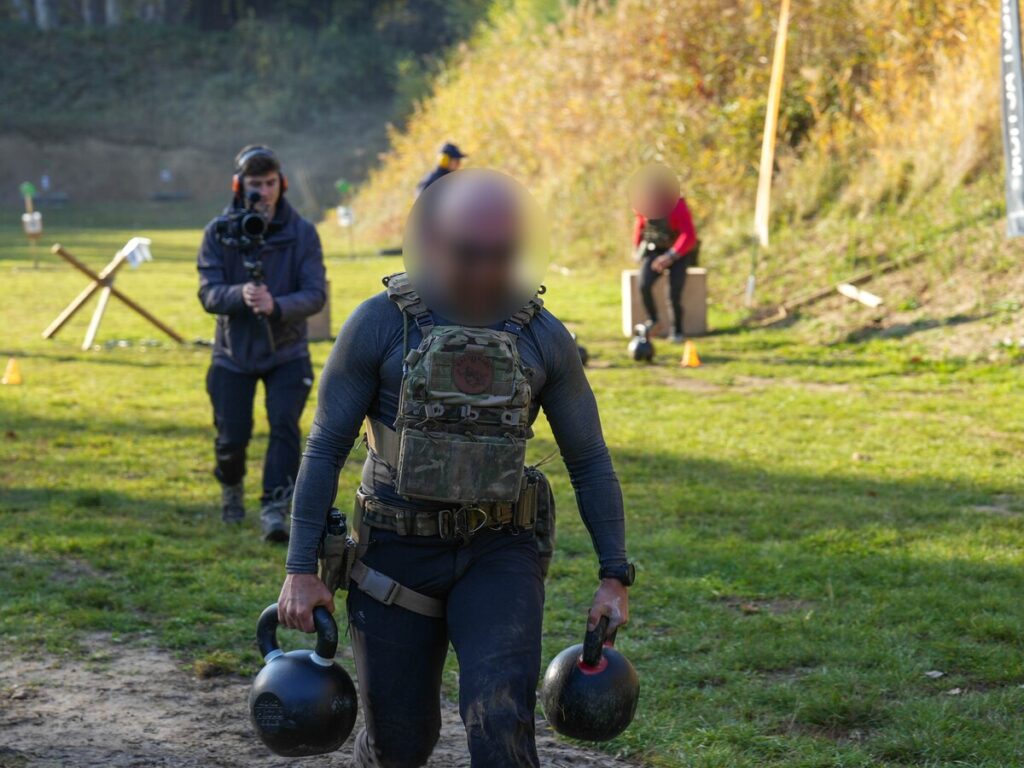 Zawodnik w kamizelce taktycznej niesie dwa odważniki podczas spaceru farmera na DRACO CHALLENGE 2026