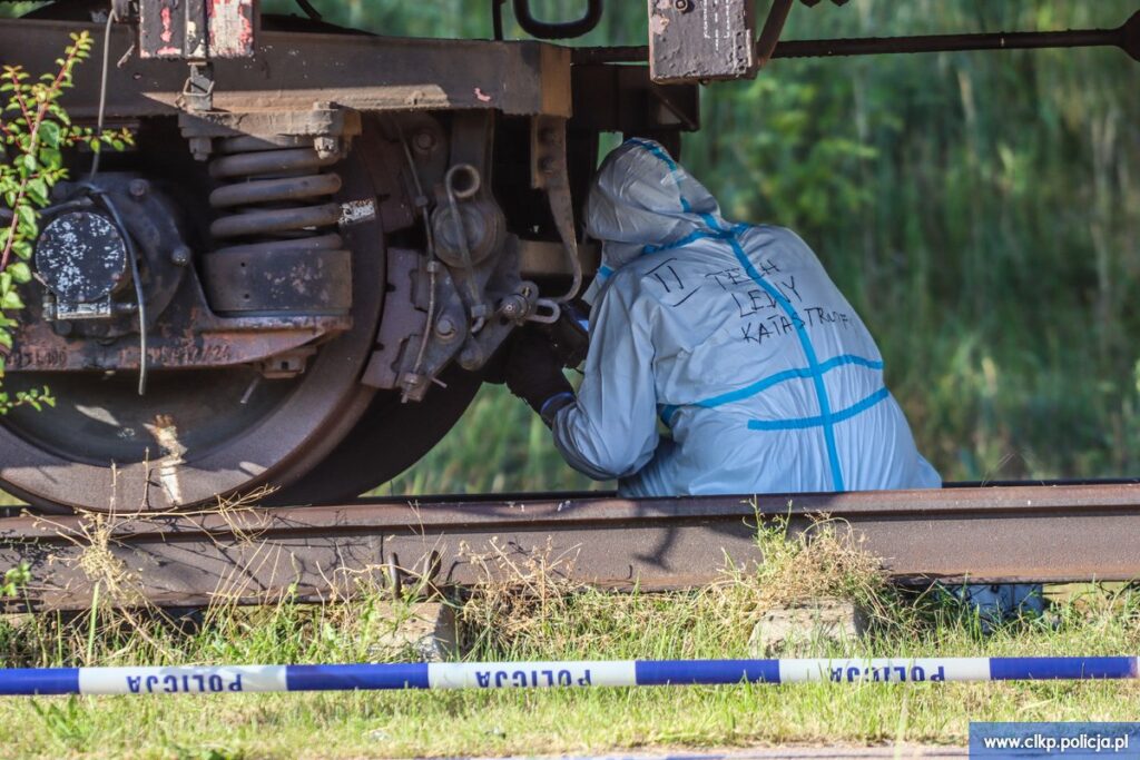 Technik w kombinezonie z napisem „Zespół ds. katastrof" kuca przy podwoziu wagonu kolejowego