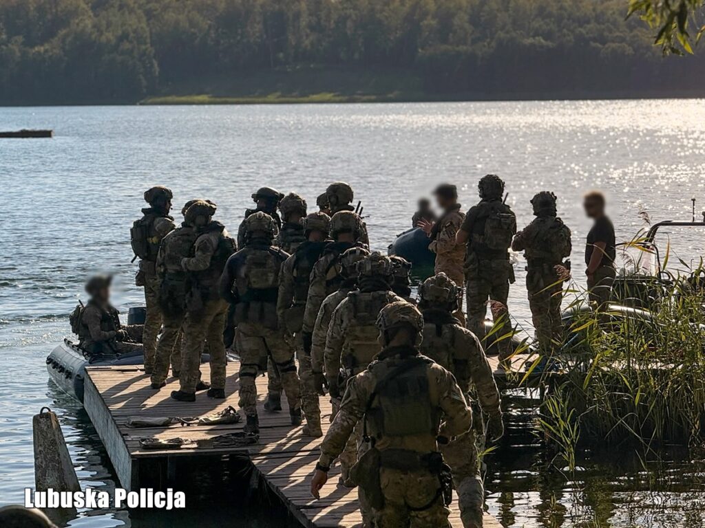 Grupa operatorów w oporządzeniu na drewnianym pomoście przy łodziach pontonowych