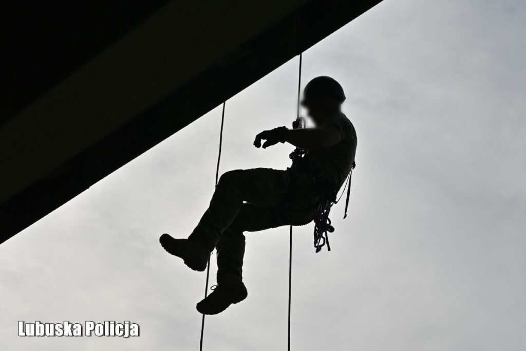 Sylwetka operatora zjeżdżającego na linie pod stalową konstrukcją na tle nieba
